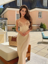 Woman in a beige evening gown with floral details standing outdoors.